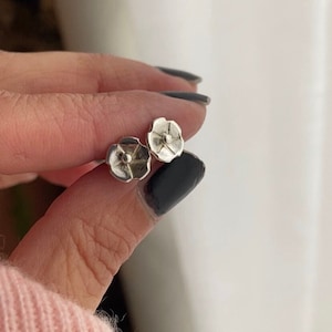 May include: A pair of silver flower-shaped stud earrings. The earrings are small and delicate, with a simple design.