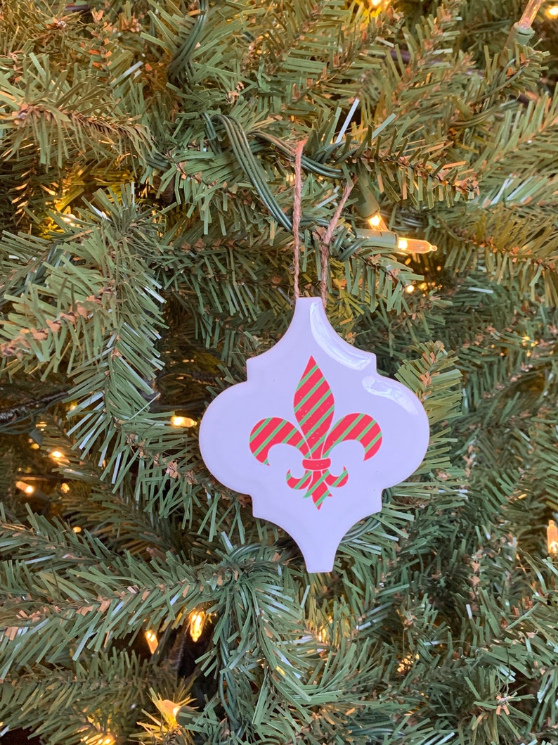 May include: A white ceramic Christmas ornament shaped like a fleur-de-lis with red and green striped accents.