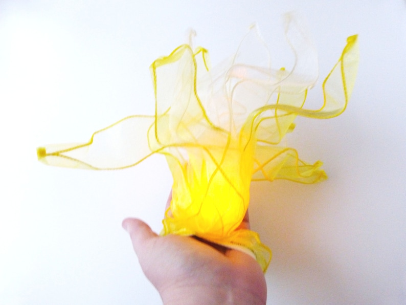 May include: A hand holding a yellow and white tulle fabric ball with a glowing light inside.