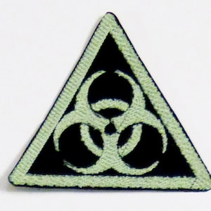 May include: A black triangular patch with a white biohazard symbol. The symbol is a stylized three-leaf clover with three circles.