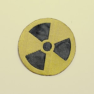 Pode incluir: Um remendo bordado amarelo e preto com um símbolo de radiação.