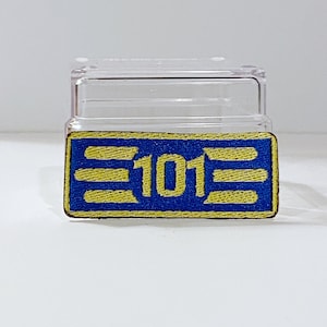 Può includere: Una toppa ricamata blu e gialla con il numero "101" al centro. La toppa è circondata da un bordo giallo.