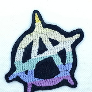 May include: A black embroidered patch with a stylized anarchy symbol in the shape of a circle. The symbol is outlined in white and filled with a rainbow color scheme, including yellow, white, light green, blue, and purple.