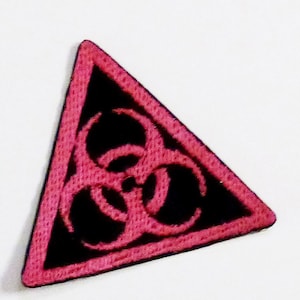 Puede incluir: Un parche de color rosa en forma de triángulo con un símbolo de riesgo biológico negro en el centro.