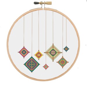 May include: A cross-stitch embroidery hoop with a white background and colorful geometric shapes hanging from the top. The shapes are in shades of green, yellow, orange, pink, and brown.