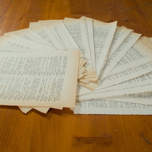 Könnte beinhalten: Ein Stapel alter, vergilbter und abgenutzter Buchseiten, die auf einer Holzoberfläche fächerförmig ausgebreitet sind.