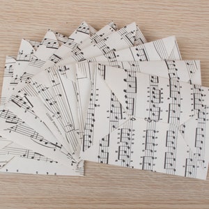 Peut inclure: Une pile d'enveloppes blanches faites de partitions de musique recyclées. Les enveloppes sont pliées et disposées en éventail. La partition de musique comporte des notes de musique noires imprimées dessus.