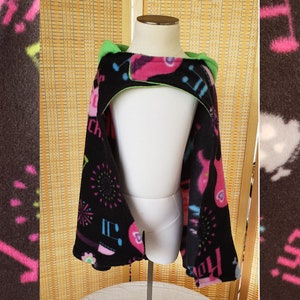 May include: Black fleece hooded poncho with a vibrant pattern of pink and blue lightning bolts, musical notes, and the word "Rock!" in pink. The hood is lined with bright green fabric.