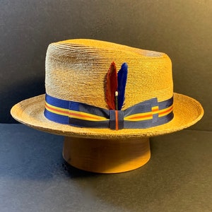 May include: A straw hat with a wide brim, blue and yellow ribbon, and a small feather accent.