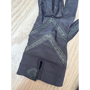 May include: A pair of dark grey gloves with decorative black leather accents. The gloves have a classic design with a small opening at the wrist and a decorative pattern on the back of the hand.