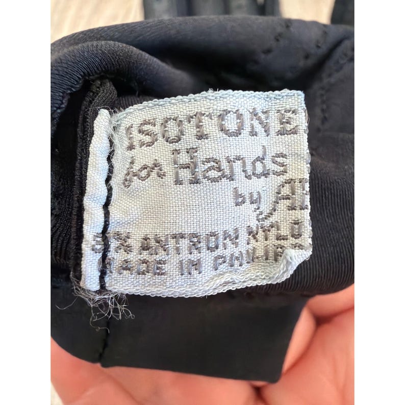 May include: Close-up of a black garment with a light blue label. The label reads "ISOTONE for Hands by A. 95% ANTRON NYLON MADE IN PHILIPPINES". The fabric appears to be a stretchy material.