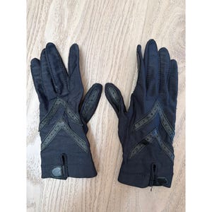 May include: A pair of navy blue gloves with chevron detailing. The gloves have a small slit at the wrist and are made of a soft material. The gloves are likely for fashion or driving. The gloves are a classic accessory.