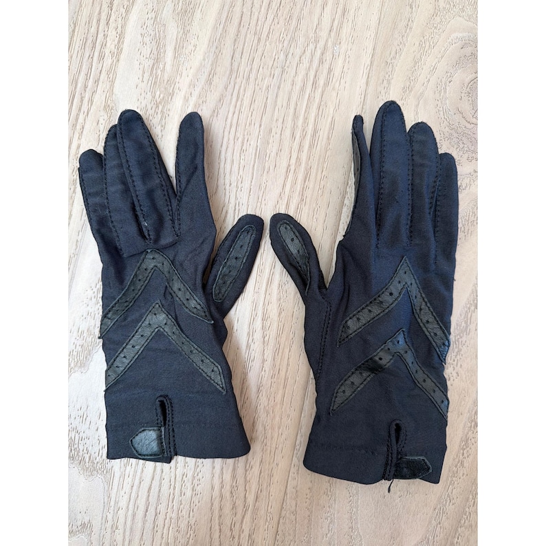 May include: A pair of navy blue gloves with chevron detailing. The gloves have a small slit at the wrist and are made of a soft material. The gloves are likely for fashion or driving. The gloves are a classic accessory.
