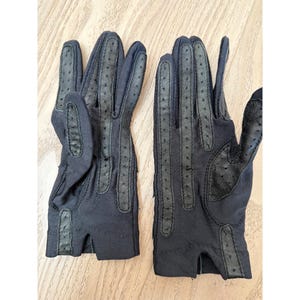 May include: A pair of black gloves with perforated leather detailing. The gloves feature a classic design with finger and palm accents. The gloves are made of a soft, dark material, suitable for driving or fashion.
