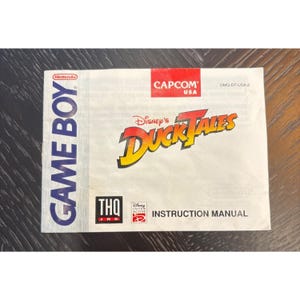 May include: A Game Boy instruction manual for Disney's DuckTales. The cover features the game's logo in yellow and orange, with the Nintendo and Capcom logos visible. The manual is white with blue and red text.