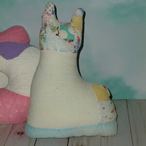 May include: A white patchwork llama stuffed animal with a blue base. The llama has a pink and purple patchwork design on its back.
