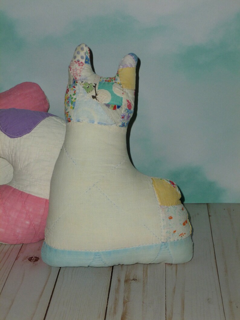 May include: A white patchwork llama stuffed animal with a blue base. The llama has a pink and purple patchwork design on its back.