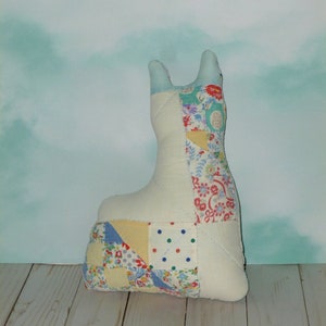 May include: A white patchwork fabric llama toy with a blue, yellow, red, and green floral pattern. The toy is sitting on a light wood surface.