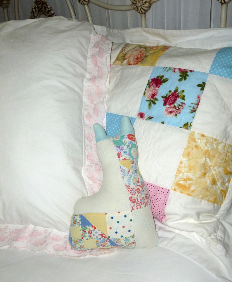 May include: A patchwork quilt with a floral design in shades of blue, pink, yellow, and white. A patchwork toy in the shape of a bunny is lying on the quilt.