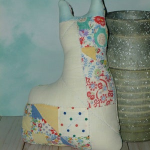 May include: A patchwork fabric cat toy with a white background and colorful floral and geometric patterns. The toy is sitting on a wooden surface next to a metal container.