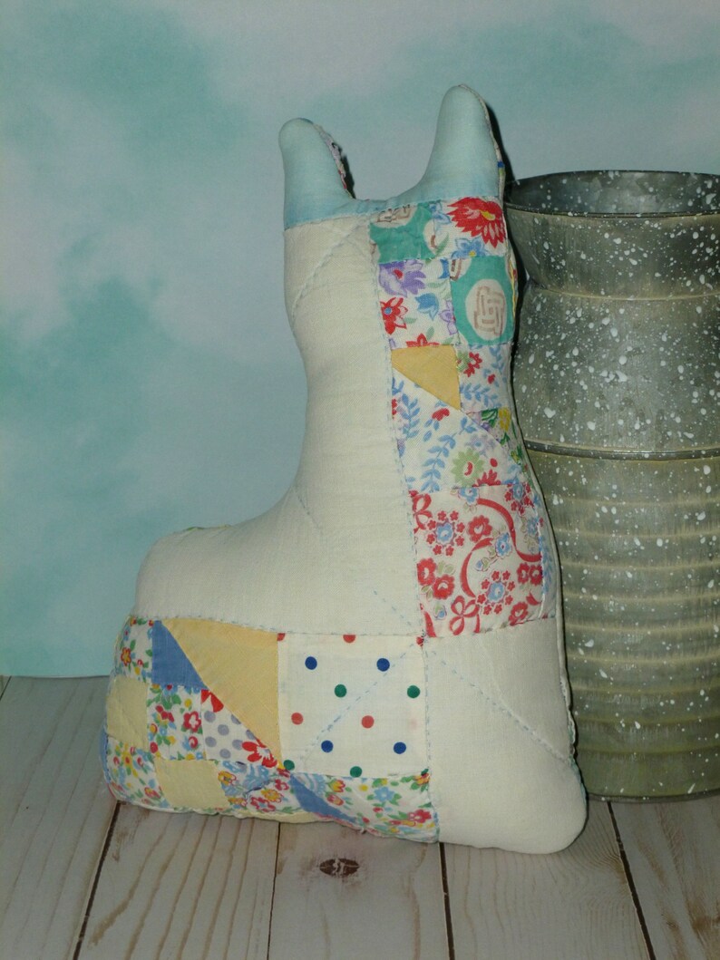 May include: A patchwork fabric cat toy with a white background and colorful floral and geometric patterns. The toy is sitting on a wooden surface next to a metal container.