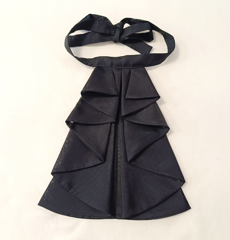 May include: A black ruffled cravat with a bow tie. The cravat is made of a soft, silky fabric and has a classic design.