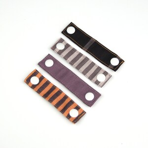 May include: Four fabric straps with white buttons. The straps are in different patterns: black, striped, and two different shades of purple.