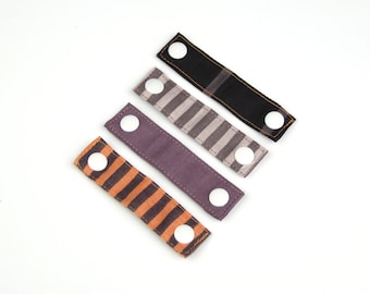 May include: Four fabric straps with white buttons. The straps are in different patterns: black, striped, and two different shades of purple.
