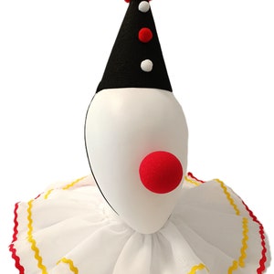 Könnte beinhalten: Ein weißer Clownskragen mit rotem und gelbem Besatz, ein schwarz-weißer, kegelförmiger Hut mit rotem Bommel und einer roten Schaumstoff-Clownsnase.