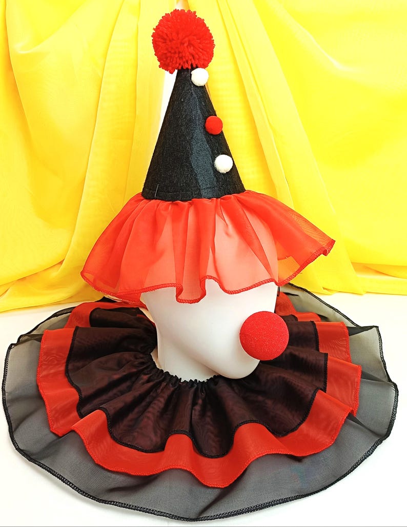 May include: A black and red clown hat with a red pom-pom on top. The hat has a red and black ruffle around the bottom. A red foam clown nose is attached to a black and red ruffle collar.