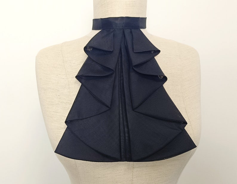 May include: A black ruffled collar with a simple band at the neck. The collar is made of a soft, flowing fabric and has a dramatic, elegant look.