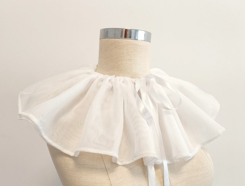 May include: A white ruffled collar with a satin ribbon tie. The collar is made of a lightweight fabric and has a delicate, feminine look.