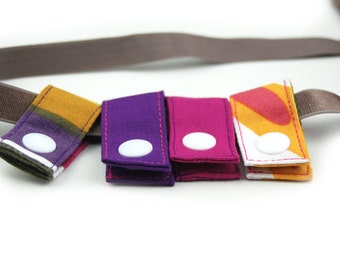 May include: Four colorful fabric straps with white buttons. The straps are folded in half and have a variety of patterns, including stripes, polka dots, and geometric shapes.