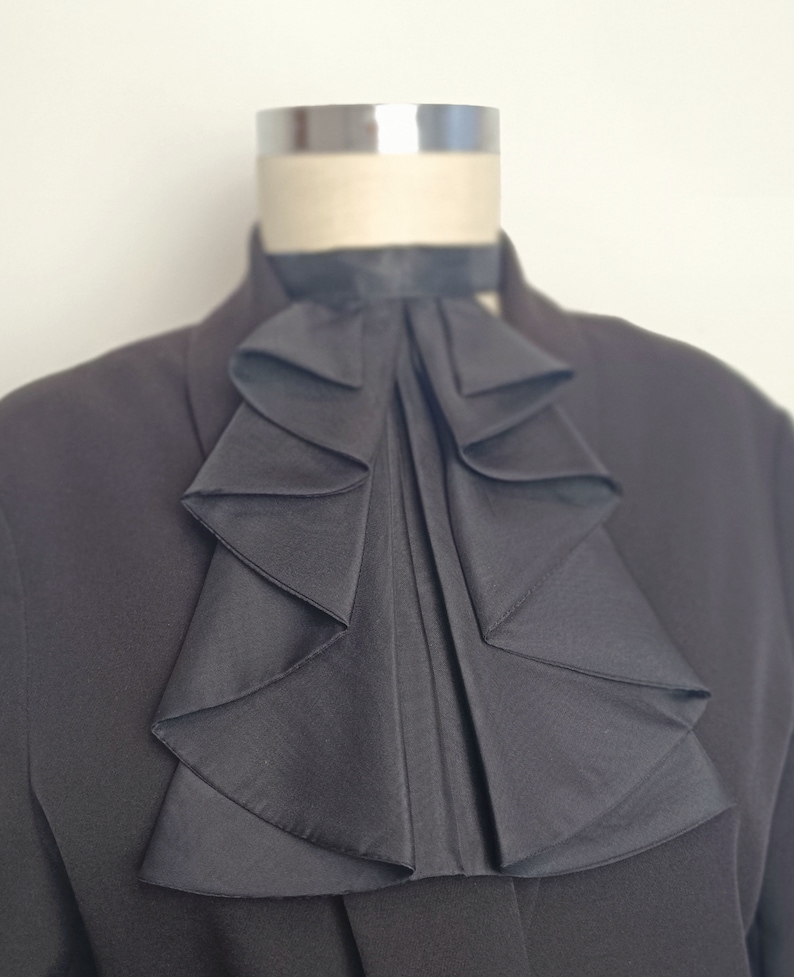May include: A black ruffled collar, worn on a dress shirt, with a formal look.