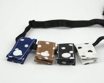 May include: Four fabric covered clips with white polka dots and white buttons. The clips are attached to a black elastic headband.