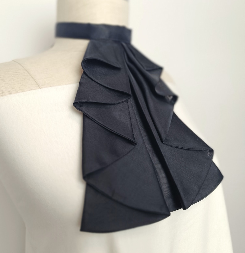 May include: A black satin ruffle collar with a high neckline. The collar is made of multiple layers of fabric and has a smooth, silky texture.
