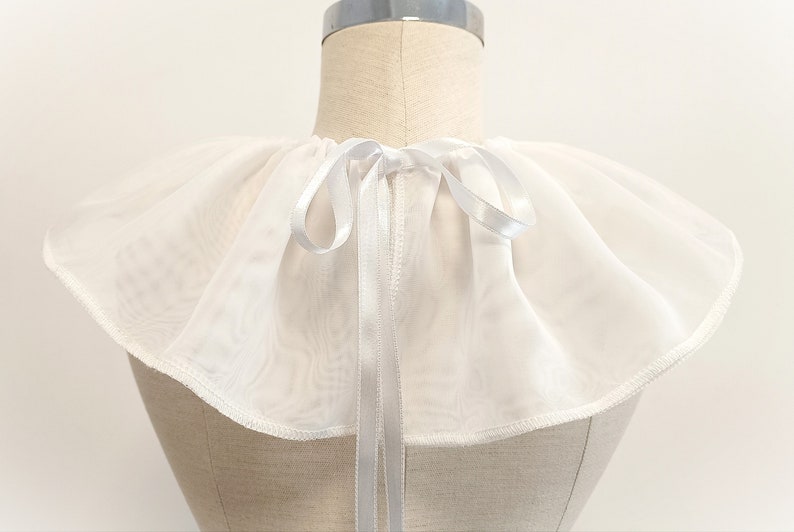 May include: White sheer ruffled collar with a white satin ribbon tie. The collar is made of a lightweight fabric and has a delicate, feminine look.