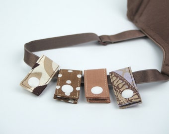 May include: Five fabric straps with white buttons, each with a different pattern in brown, beige, and white. The straps are attached to a brown elastic band.