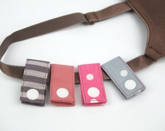 May include: Five fabric straps with white buttons, each with a different pattern: striped, solid pink, polka dot, and gray with white polka dots. The straps are attached to a brown strap.
