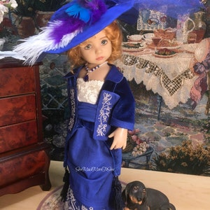 May include: A doll wearing a blue velvet dress with silver embroidery and a matching blue hat with feathers. The doll has blonde hair and blue eyes. The doll is standing next to a small black dog figurine.