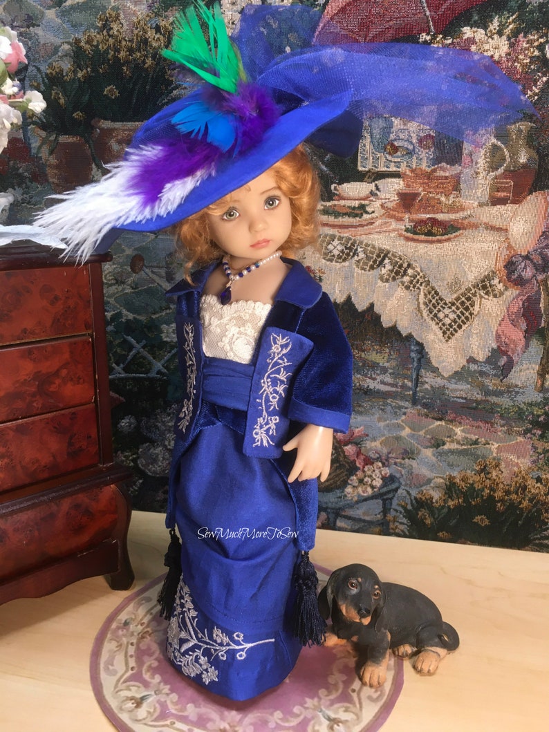 May include: A doll wearing a blue velvet dress with silver embroidery and a matching blue hat with feathers. The doll has blonde hair and blue eyes. The doll is standing next to a small black dog figurine.