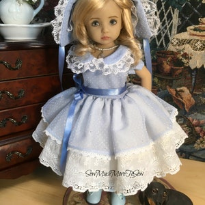 May include: A porcelain doll wearing a light blue dress with white polka dots and lace trim. The doll has blonde hair and blue eyes. The doll is wearing a blue ribbon around her waist and a white lace bonnet. The doll is standing on a rug with a small black dachshund figurine beside her.
