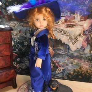 May include: A porcelain doll wearing a blue velvet dress with a white lace trim and a blue hat with feathers. The doll is standing on a pink and white rug with a small black dachshund figurine.