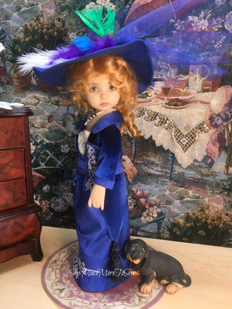 May include: A porcelain doll wearing a blue velvet dress with a white lace trim and a blue hat with feathers. The doll is standing on a pink and white rug with a small black dachshund figurine.