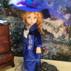 May include: A porcelain doll wearing a blue velvet dress with silver embroidery and a blue hat with a white and purple feather. The doll is standing on a rug with a small black dachshund figurine beside it.