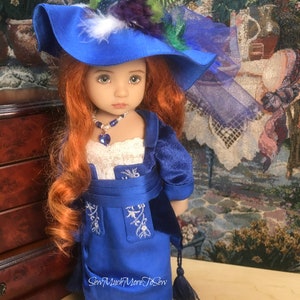 May include: A doll wearing a blue dress with white embroidery and a blue hat with feathers. The doll has long red hair and blue eyes. The doll is wearing a necklace with a blue gem.