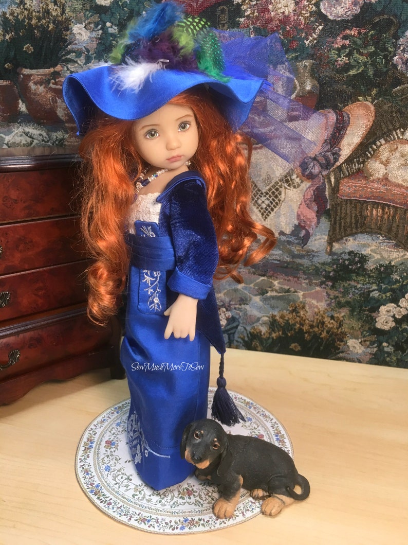 May include: A porcelain doll wearing a blue velvet jacket and a blue satin dress with white embroidery. The doll has long red hair and is wearing a blue hat with feathers. The doll is standing on a round, white, floral patterned surface with a black dachshund figurine.