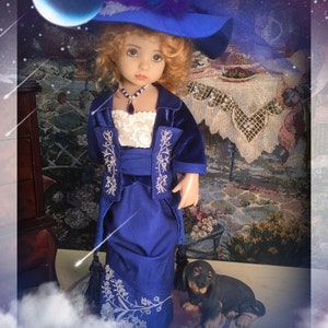 May include: A porcelain doll wearing a blue velvet dress with white embroidery and a blue hat. The doll has blonde hair and blue eyes. The doll is standing on a white cloud-like surface with a small brown and black dog figurine beside it.