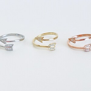 May include: Three adjustable rings with a double arrow design. The rings are silver, gold, and rose gold.