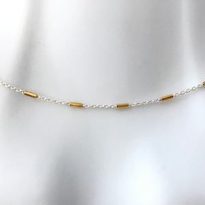 May include: A silver chain necklace with gold bar accents.